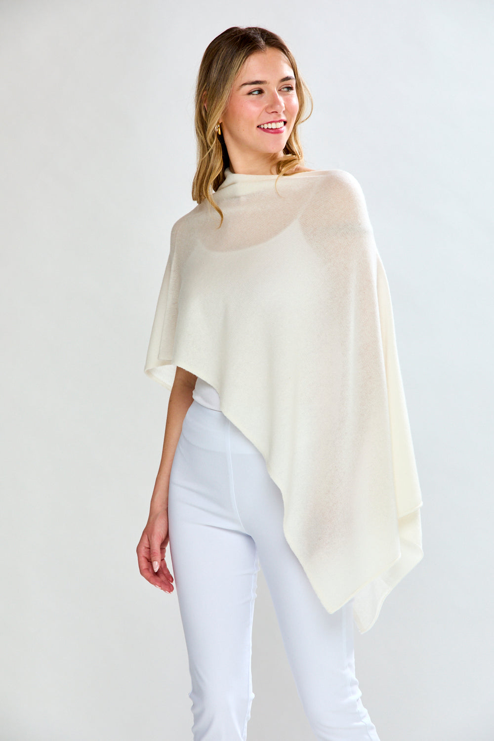 Woman wearing a cream-colored poncho over a white outfit on a plain background
