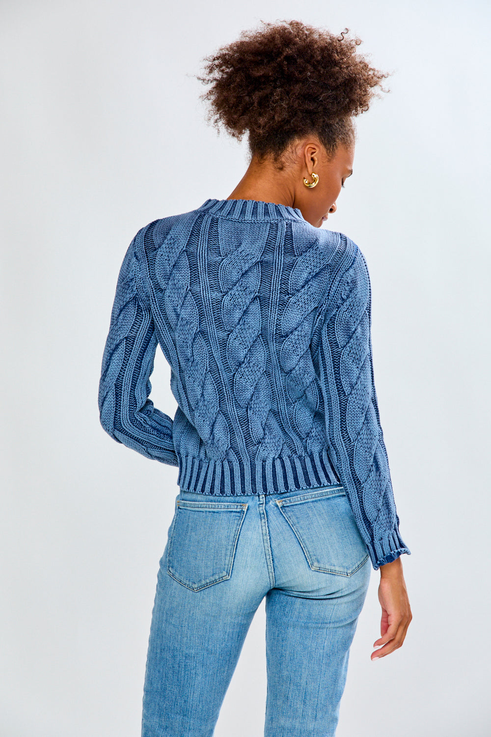 Woman wearing a denim cable knit sweater and blue jeans on a white background