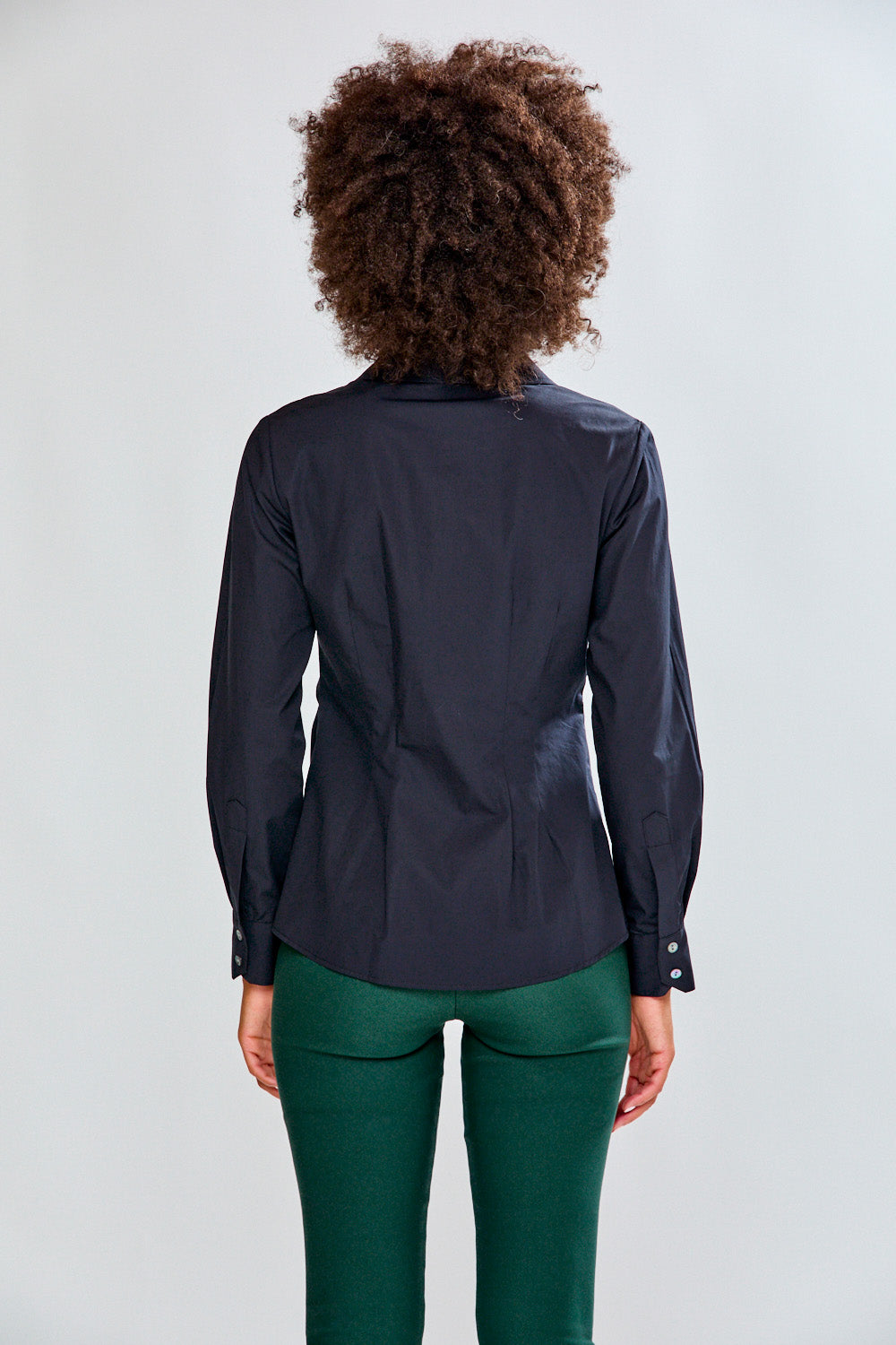 Person wearing a black blouse and green pants against a white background
