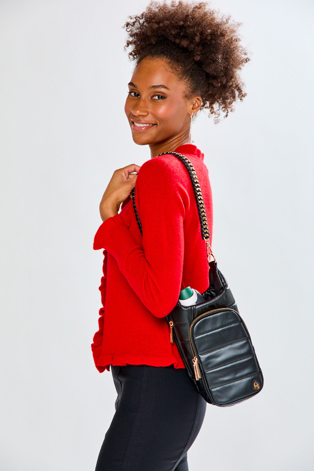 Woman with black leather crossbody water bottle bag with gold chain detail on a white background