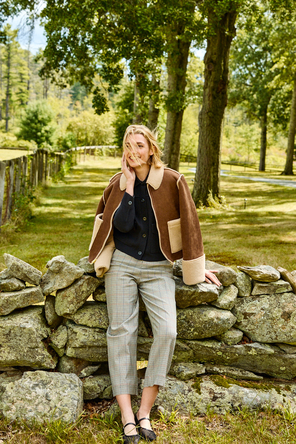Woman standing by a stone wall in a park-like setting
