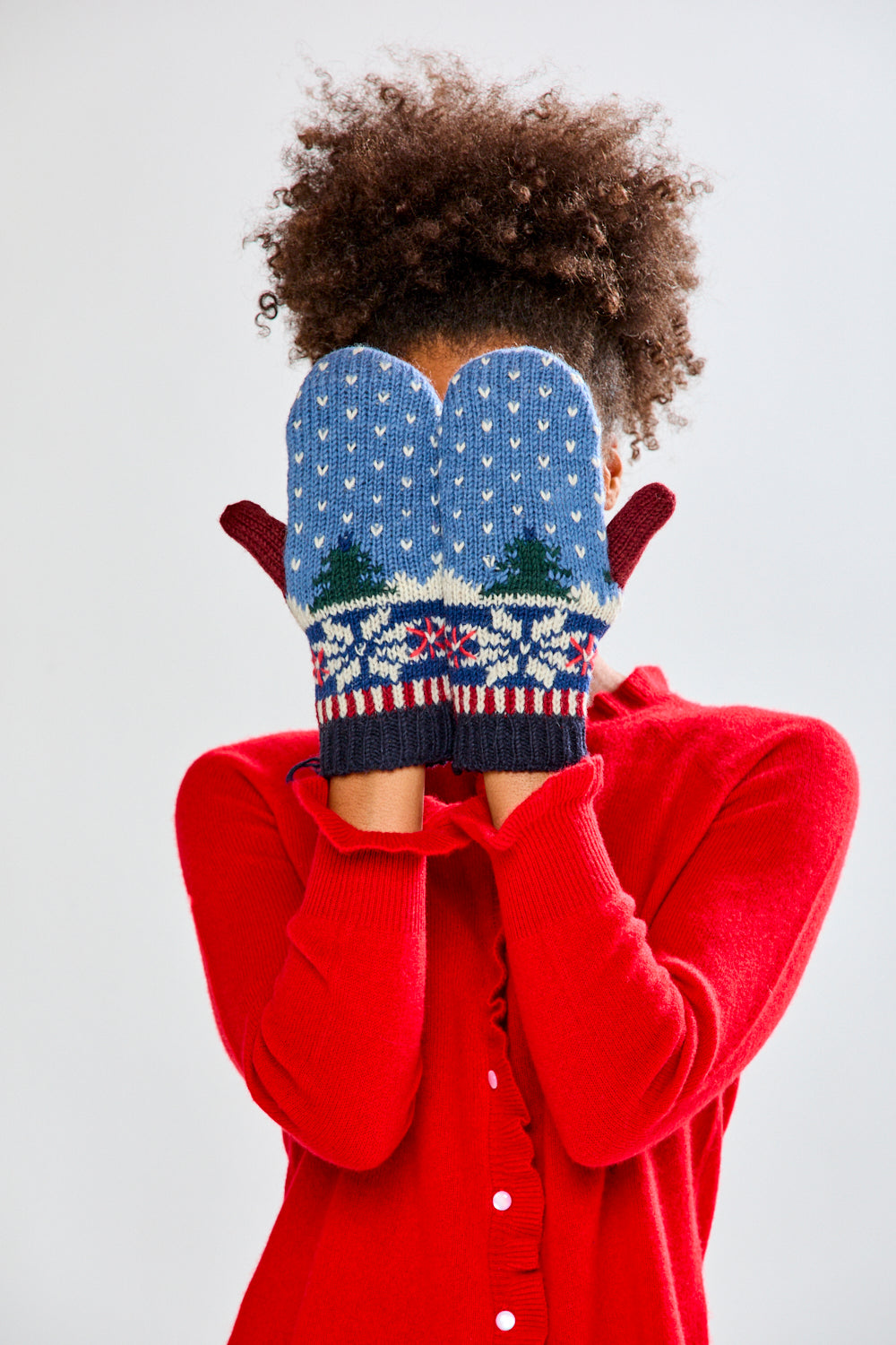 Woman wearing a red sweater and festive mittens on a plain background