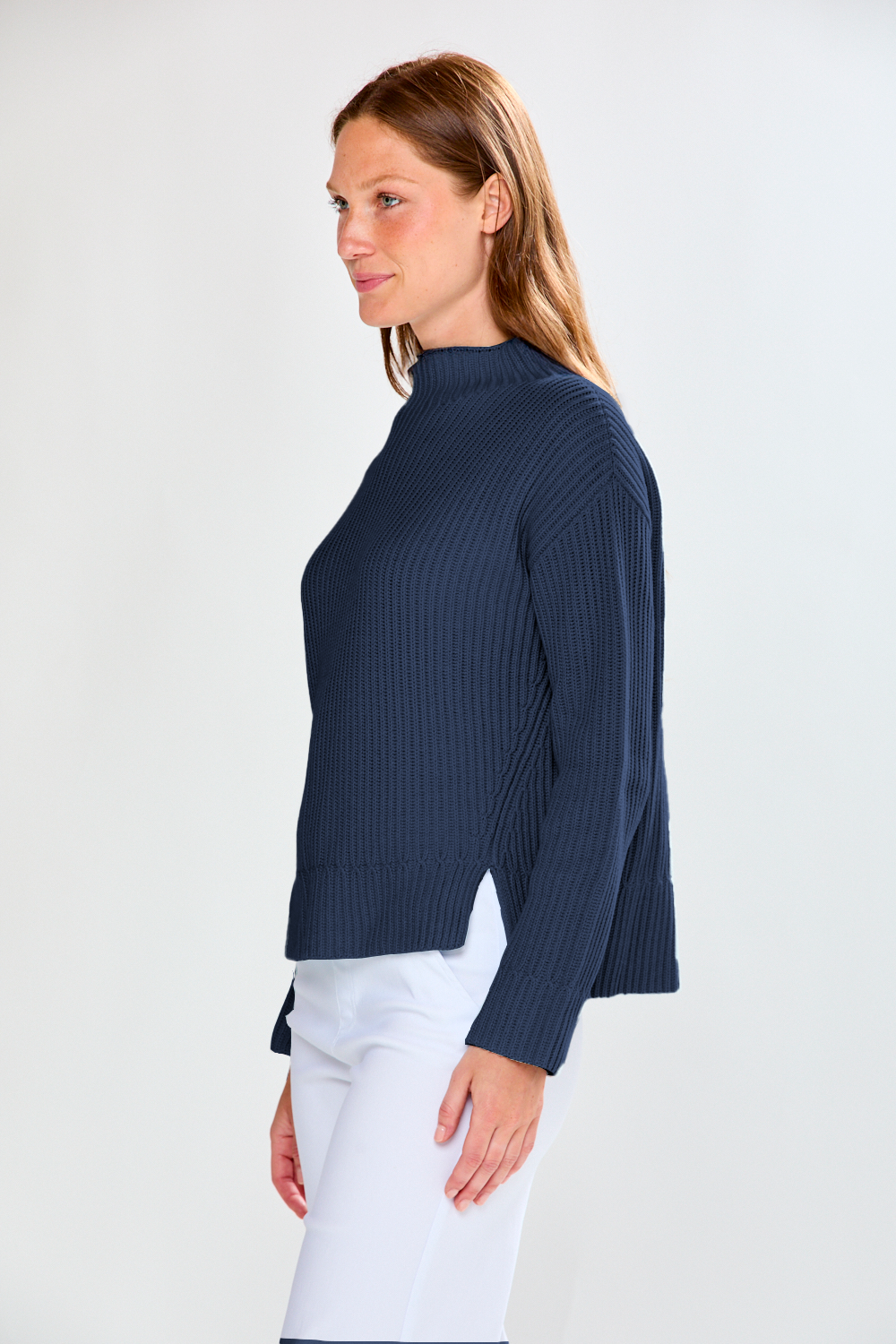 Woman wearing a navy ribbed sweater and white pants on a plain background