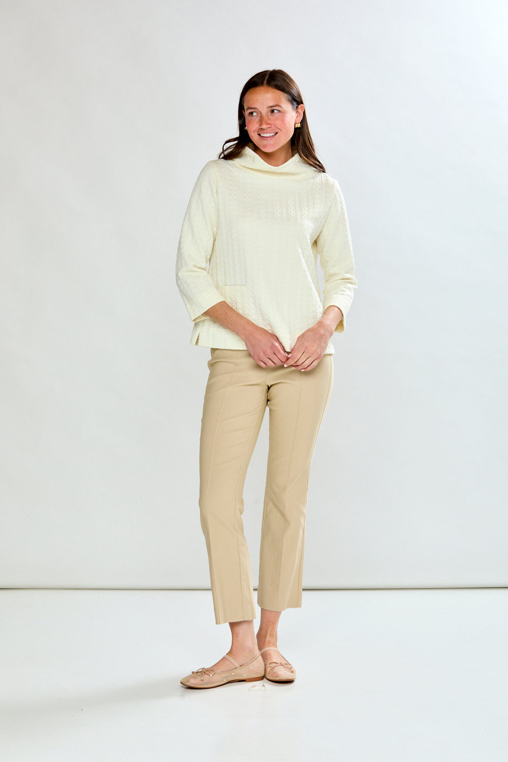 Woman wearing a ivory top and beige pants against a white background