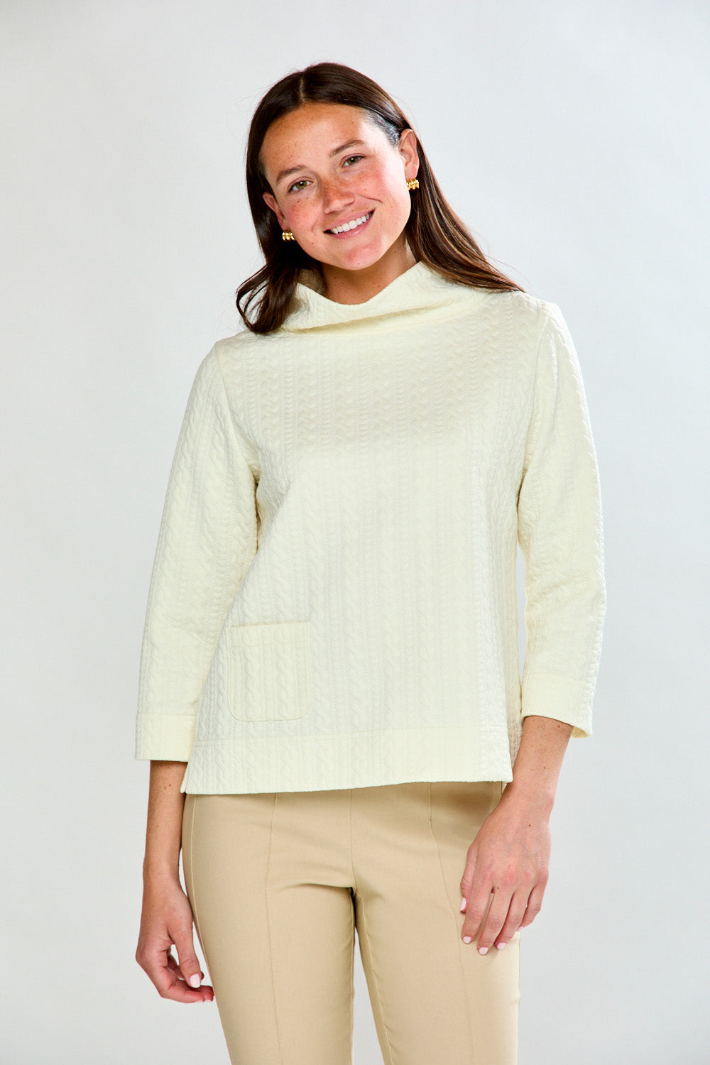 Woman wearing a ivory top and beige pants against a white background