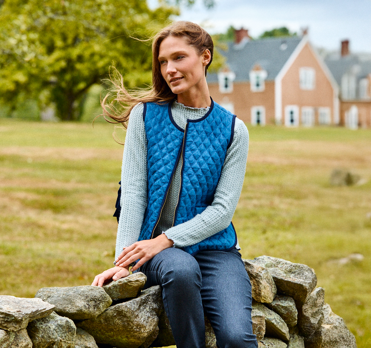 Woman wearing a blue vest while sitting on a stone wall