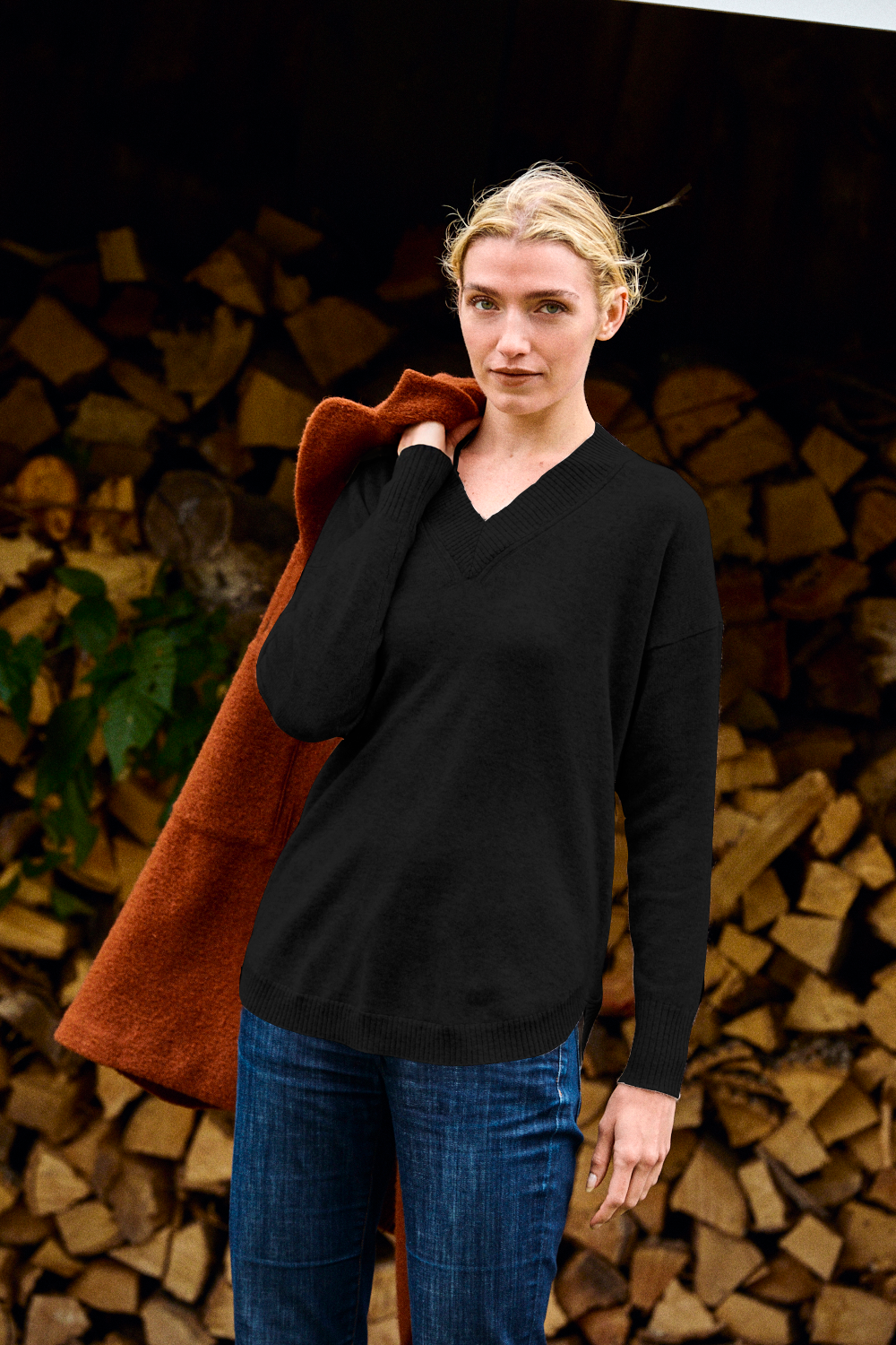 Woman wearing a black v neck sweater with a brown coat over her shoulder.