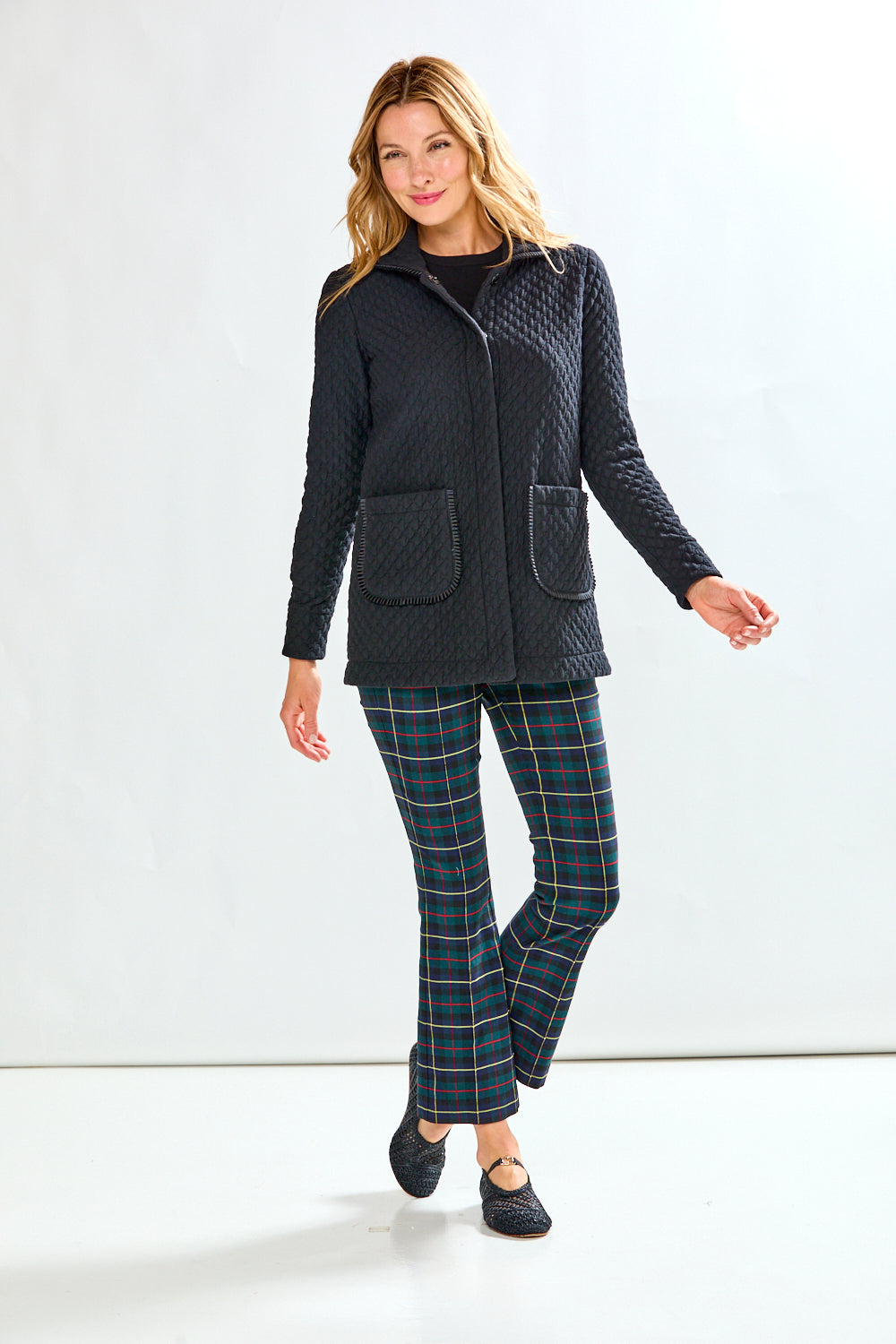 Woman wearing a black quilted jacket and plaid pants on a white background