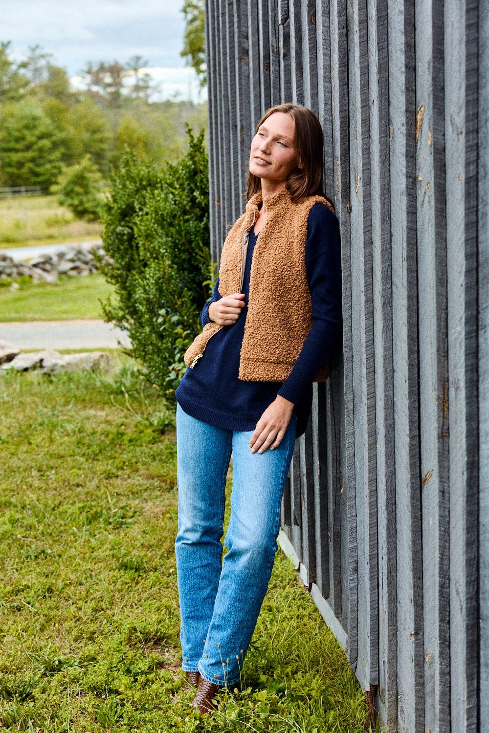 Woman wearing navy sweater, brown vest, and jeans.