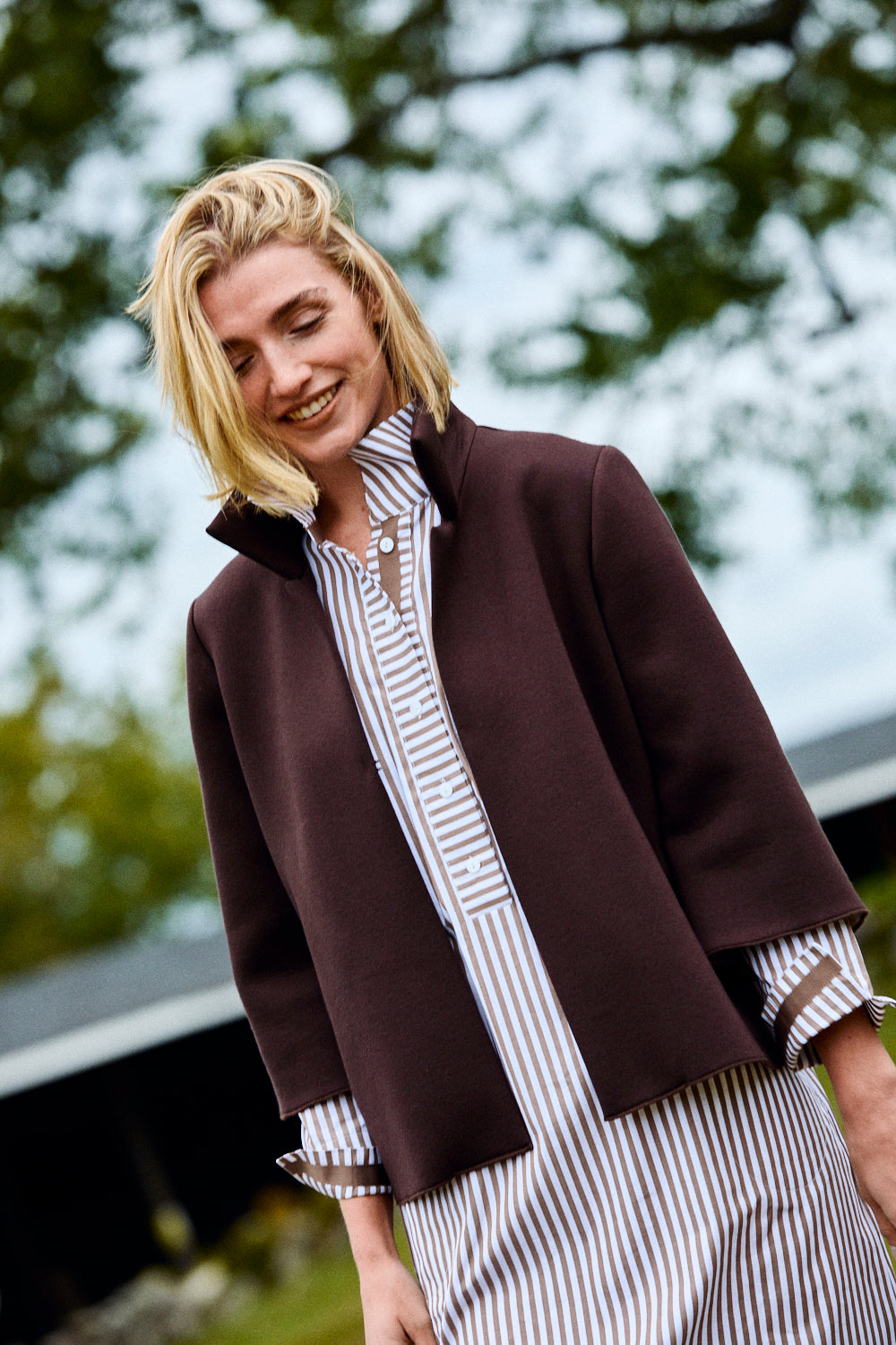 Woman wearing a brown coat over a striped shirt and pants outdoors