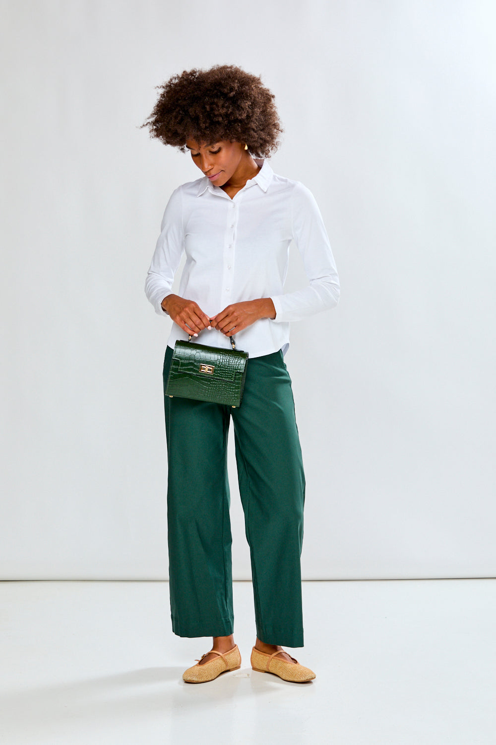Woman wearing a white shirt and green pants against a plain background