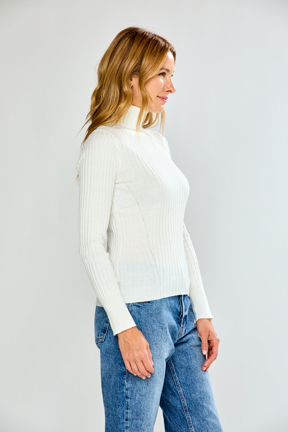 Woman wearing a white turtleneck sweater and blue jeans on a plain background