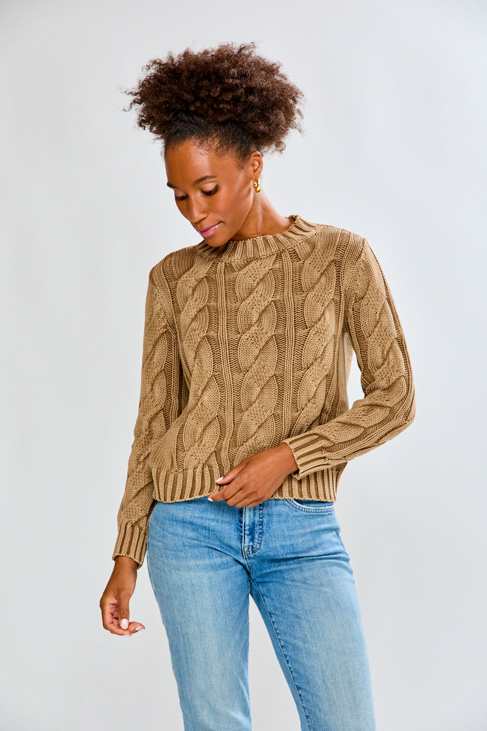 Woman wearing a toffee cable knit sweater and blue jeans on a white background