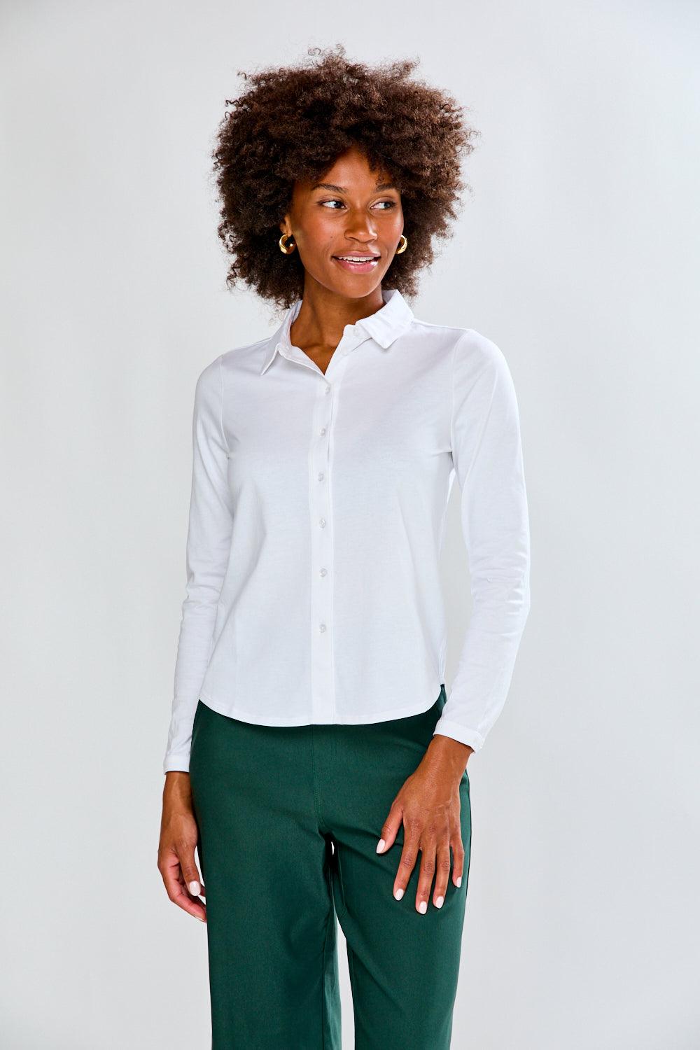 Woman wearing a white shirt and green pants against a plain background