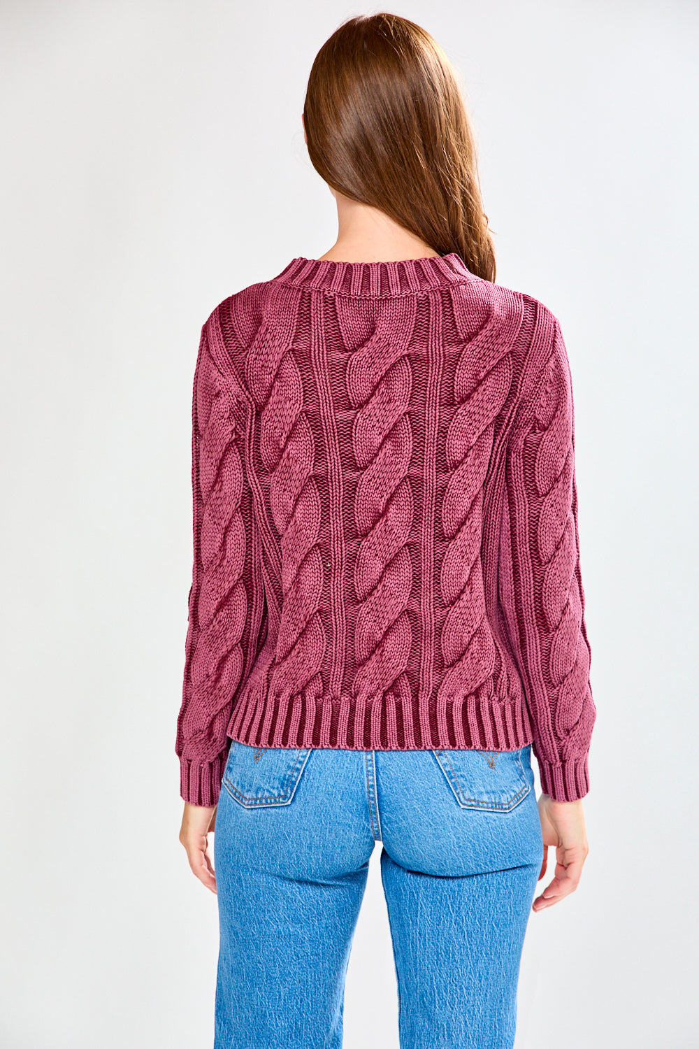 Woman wearing a raisin cable knit sweater and blue jeans on a white background