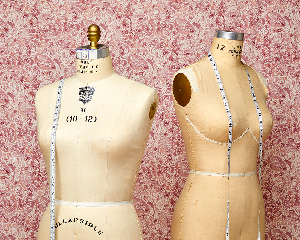 Two dress forms with measuring tape around the shoulders
