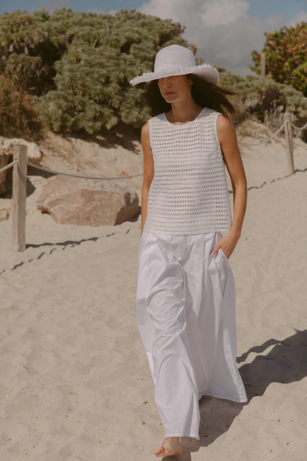 Woman in a white basket weave shirt and white cotten pants while on the beach.