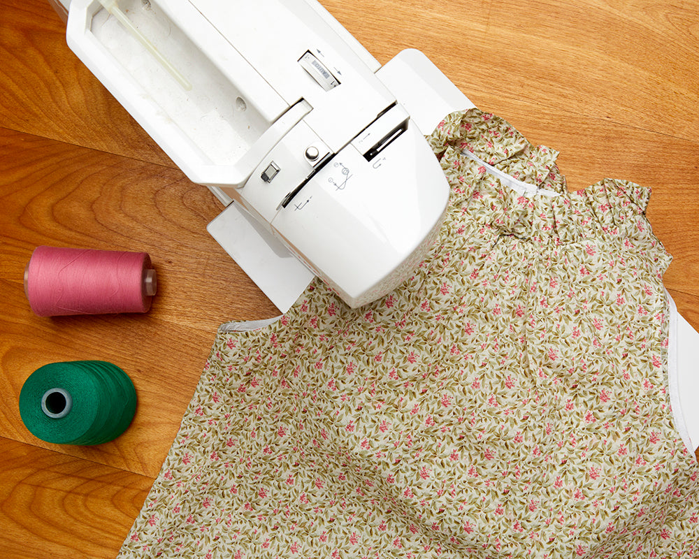 Sewing machine stitching a dress with two spools of thread laying on the table.