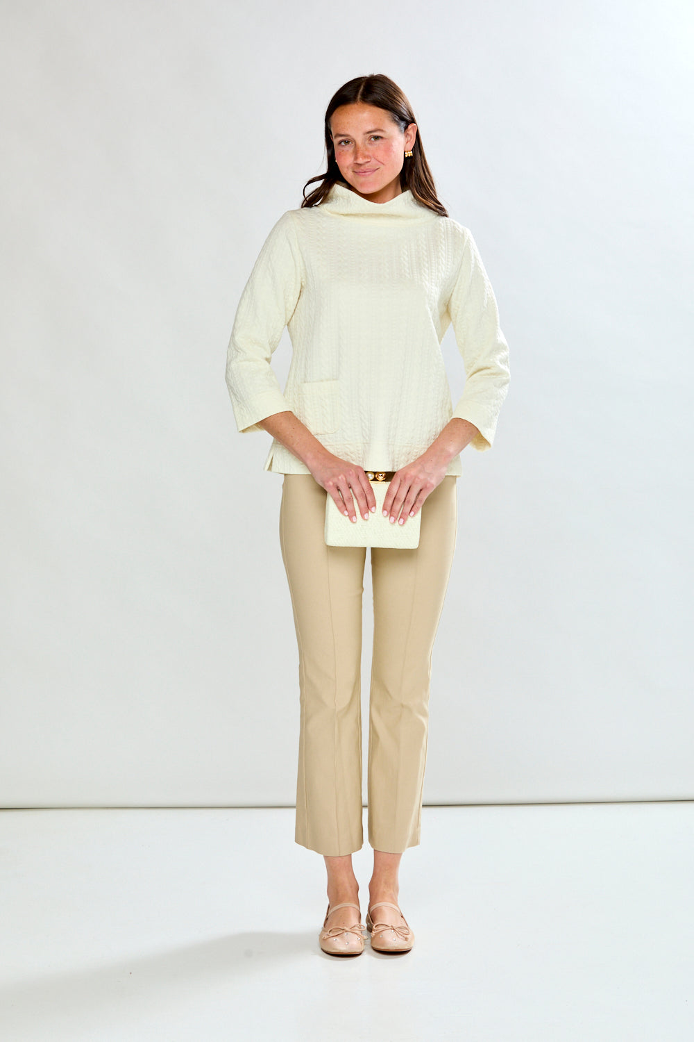 Woman wearing a ivory top and beige pants against a white background