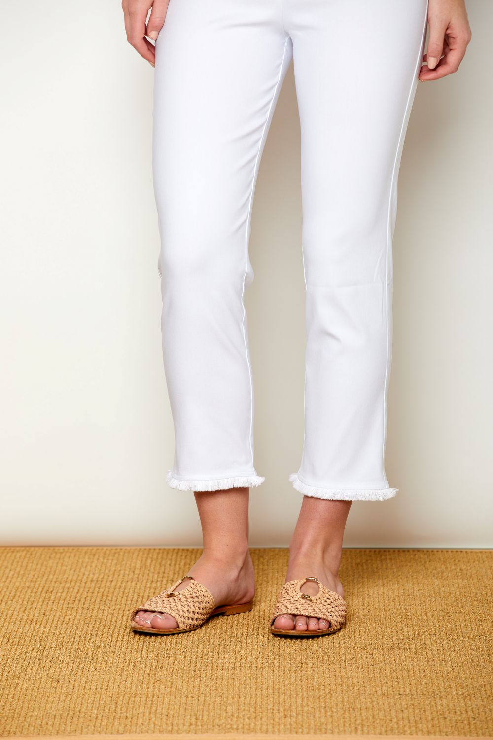 Person wearing white pants and brown sandals on a beige floor.
