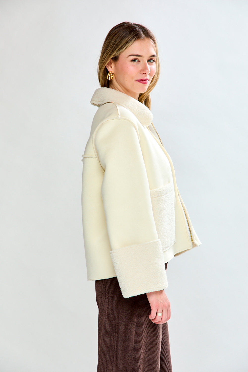 Woman wearing a cream-colored coat over a beige sweater and brown pants on a white background