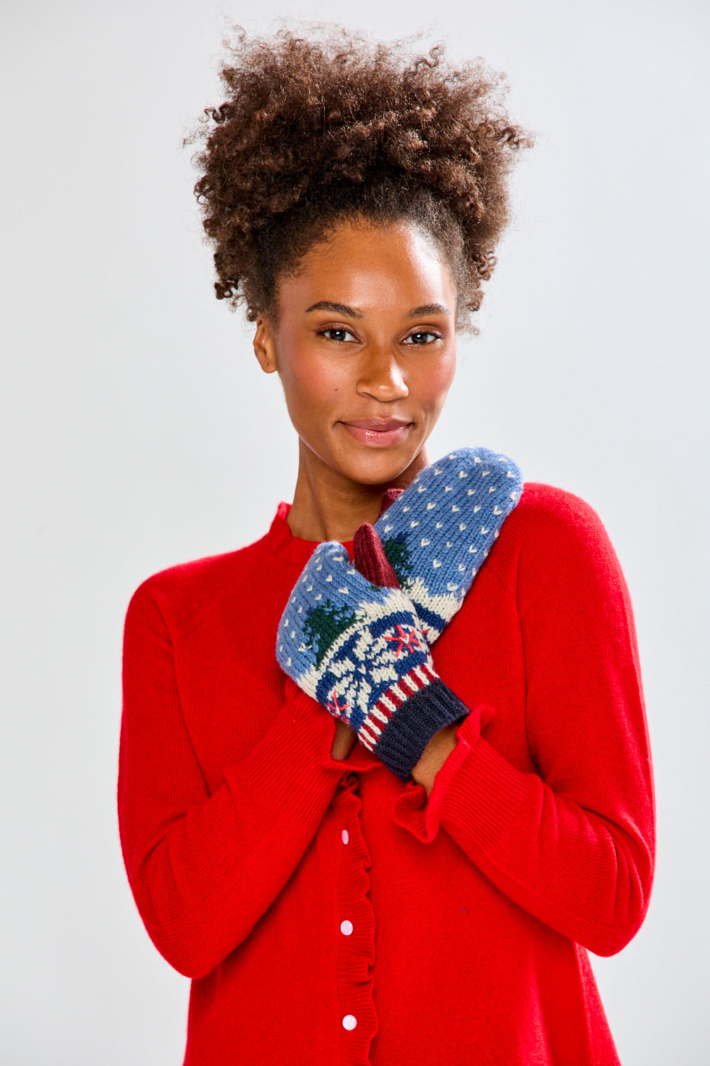 Woman wearing a red sweater and festive mittens on a plain background