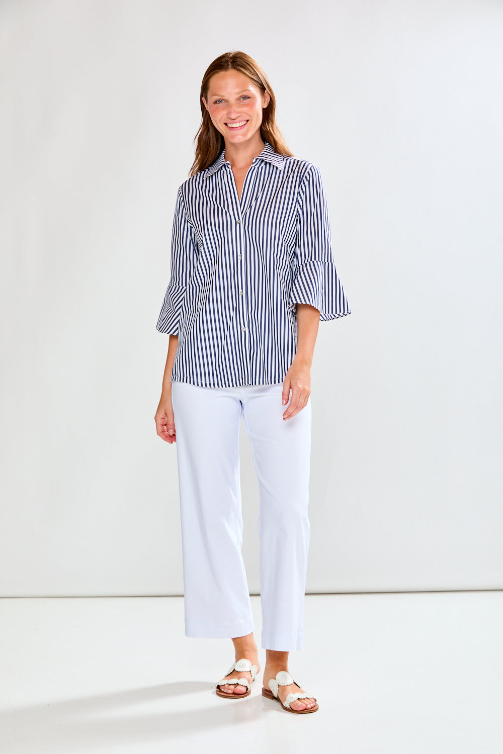 Woman wearing a striped shirt and white pants against a plain background