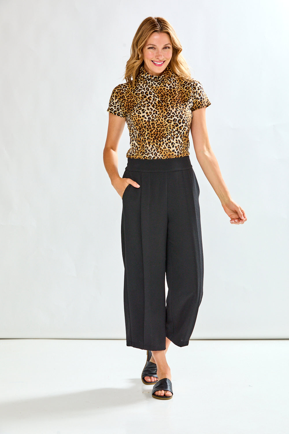 Person wearing black wide-leg pants with a leopard print top on a white background