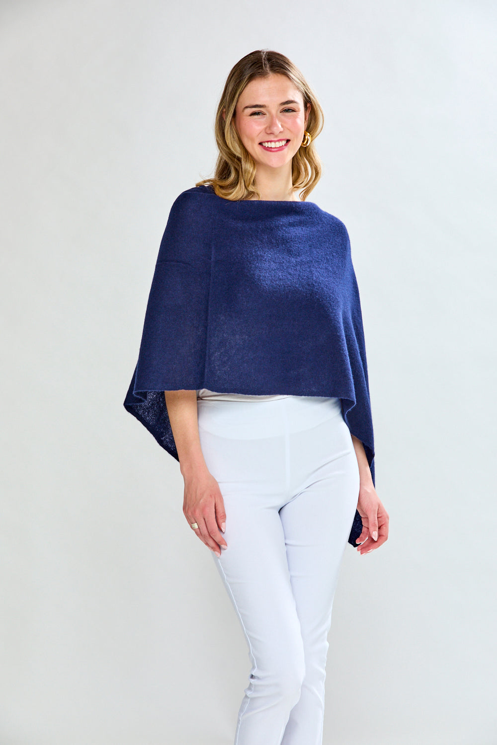 Woman wearing a navy blue poncho over a white top and pants on a light gray background
