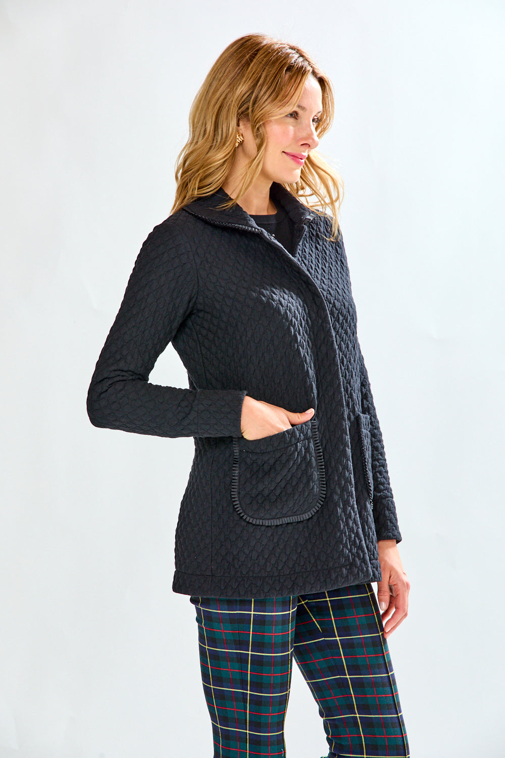 Woman wearing a black quilted jacket and plaid pants on a white background