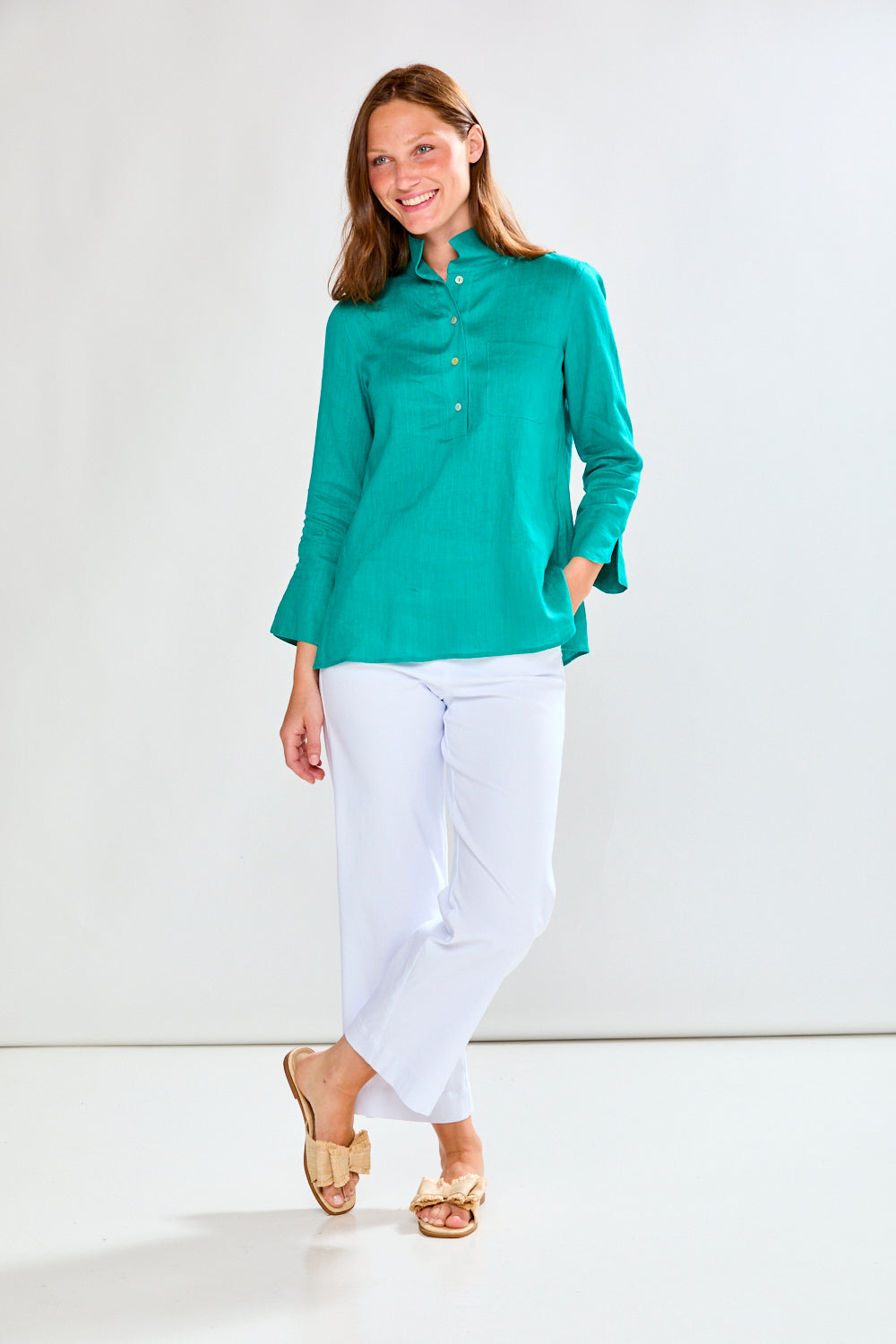 Woman wearing a teal shirt and white pants against a white background