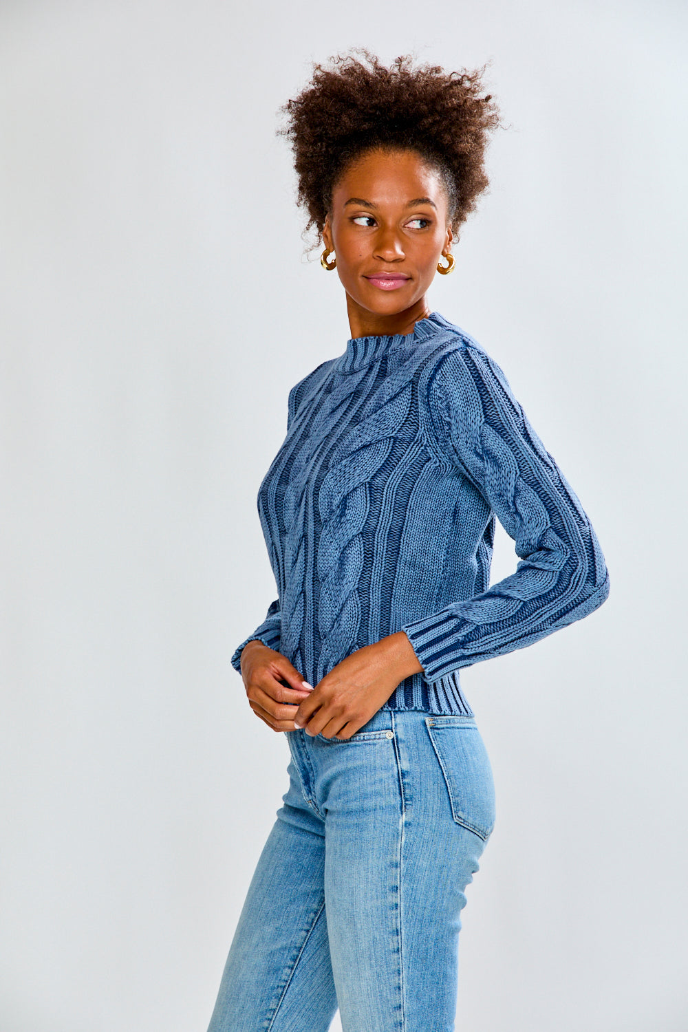 Woman wearing a denim cable knit sweater and blue jeans on a white background