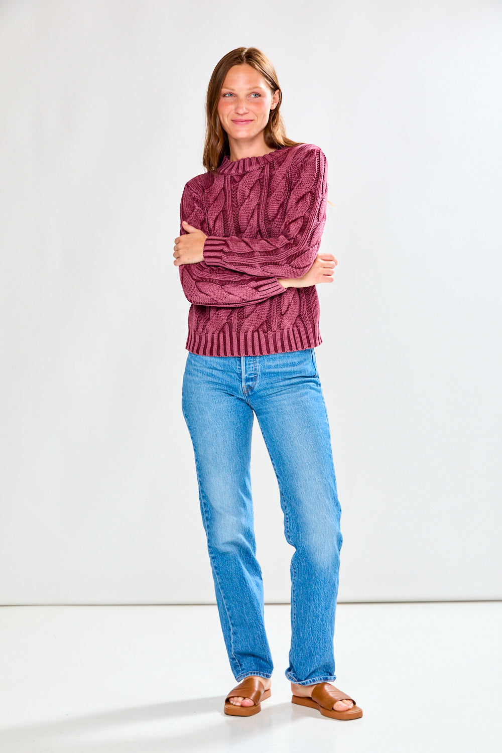Woman wearing a raisin cable knit sweater and blue jeans on a white background