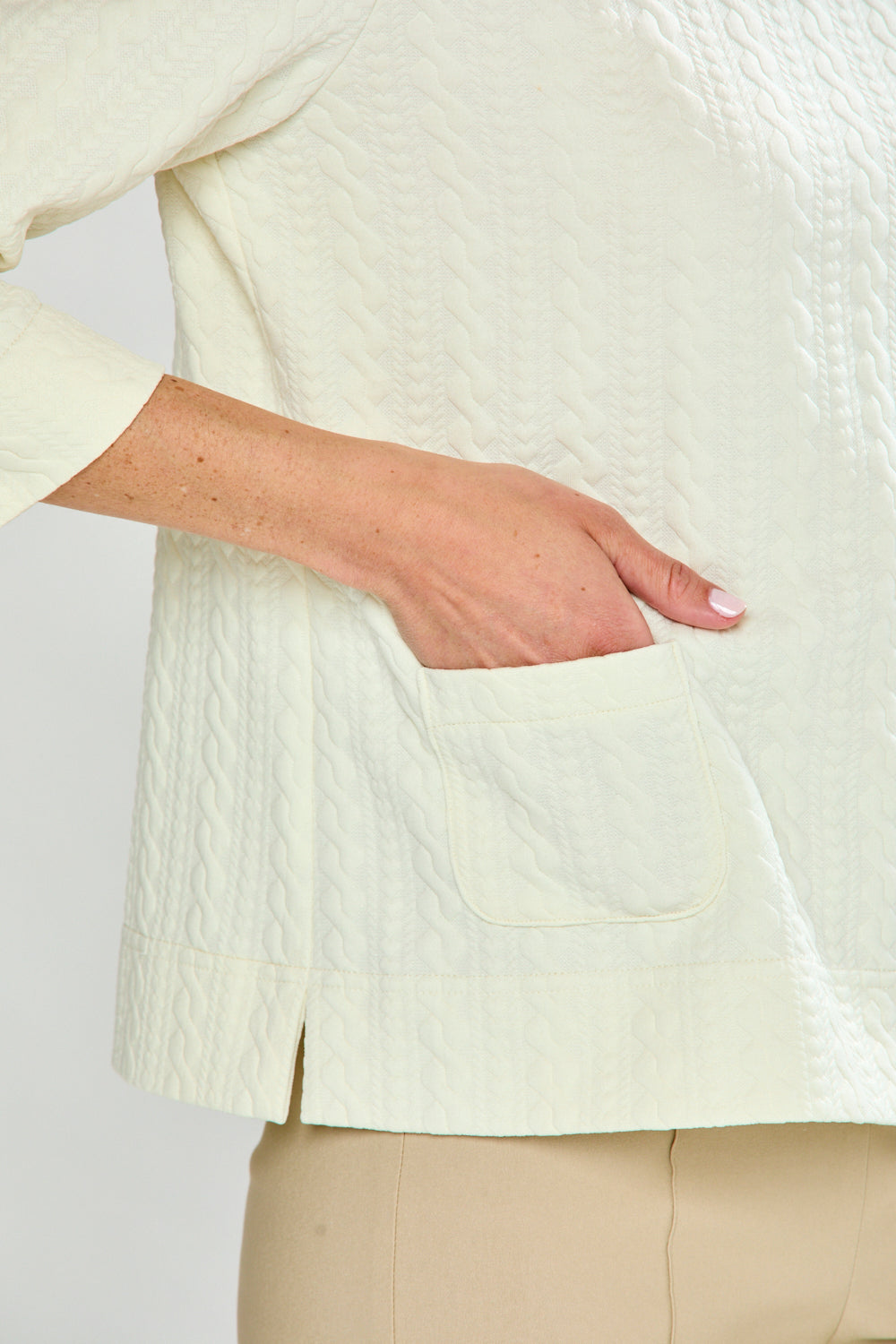 Woman wearing a ivory top and beige pants against a white background