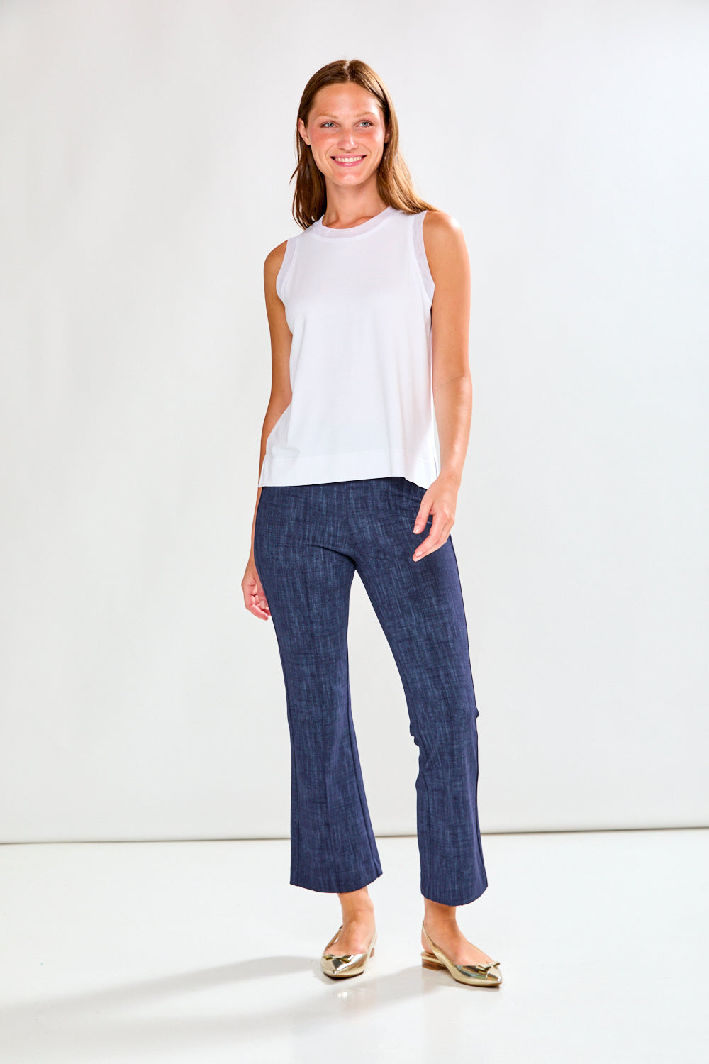 Woman wearing a white sleeveless top and blue jeans on a white background