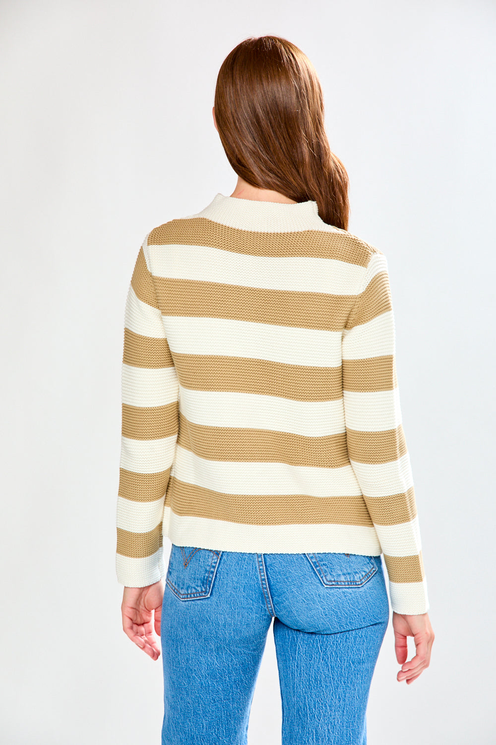 Person wearing a striped sweater and blue jeans on a plain background