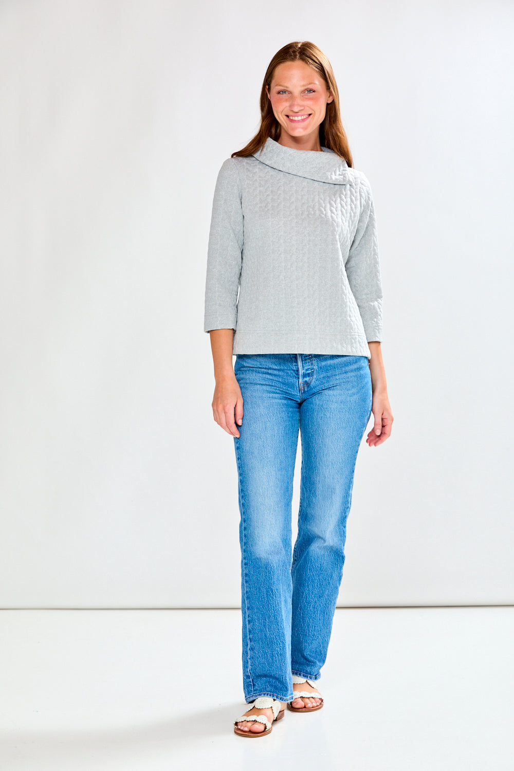 Woman wearing a light gray sweater and blue jeans on a white background