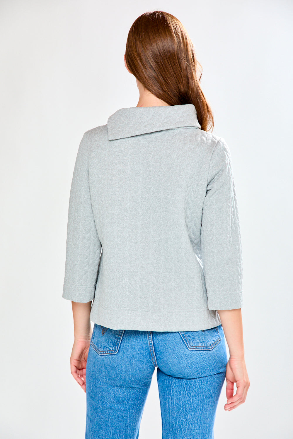 Person wearing a light gray blazer and blue jeans on a white background