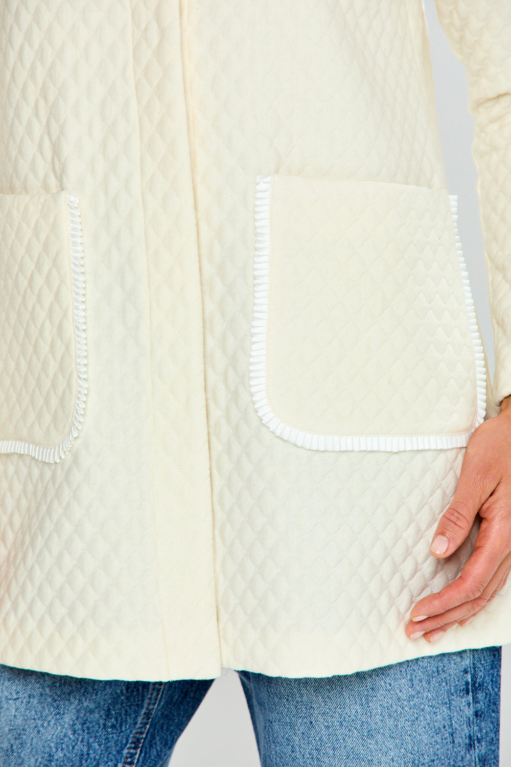 Close-up of a cream-colored quilted jacket with white trim on a neutral background