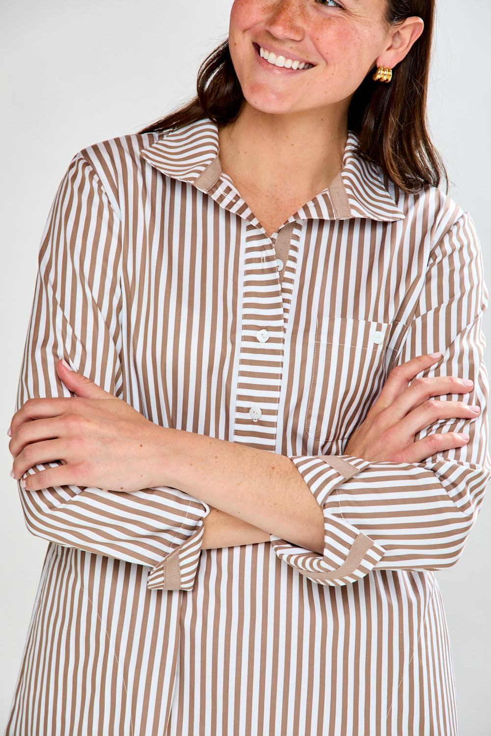 Woman wearing a brown and white striped shirt with arms crossed against a white background