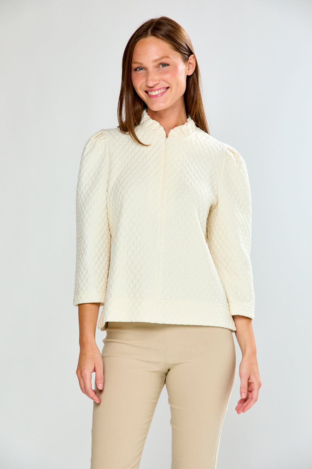 Woman wearing a cream-colored knit jacket and beige pants on a white background