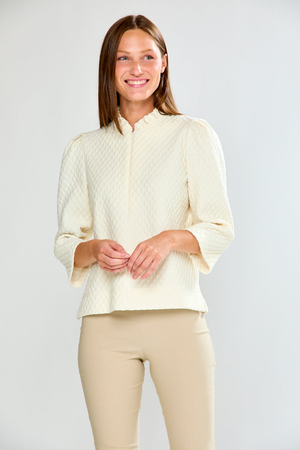 Woman wearing a light-colored sweater and beige pants against a white background