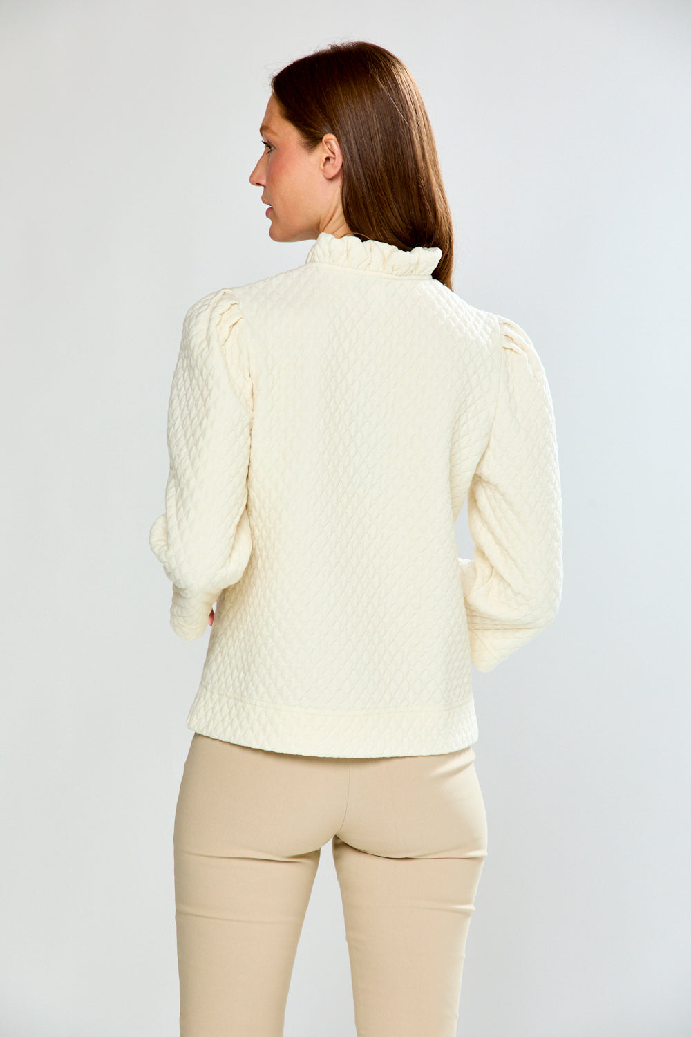 Woman wearing a light-colored blouse and beige pants against a plain background