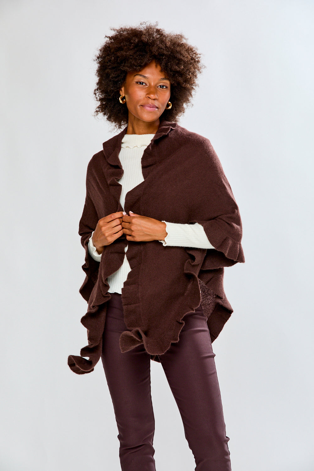 Woman wearing a brown poncho over a white shirt and purple pants on a white background