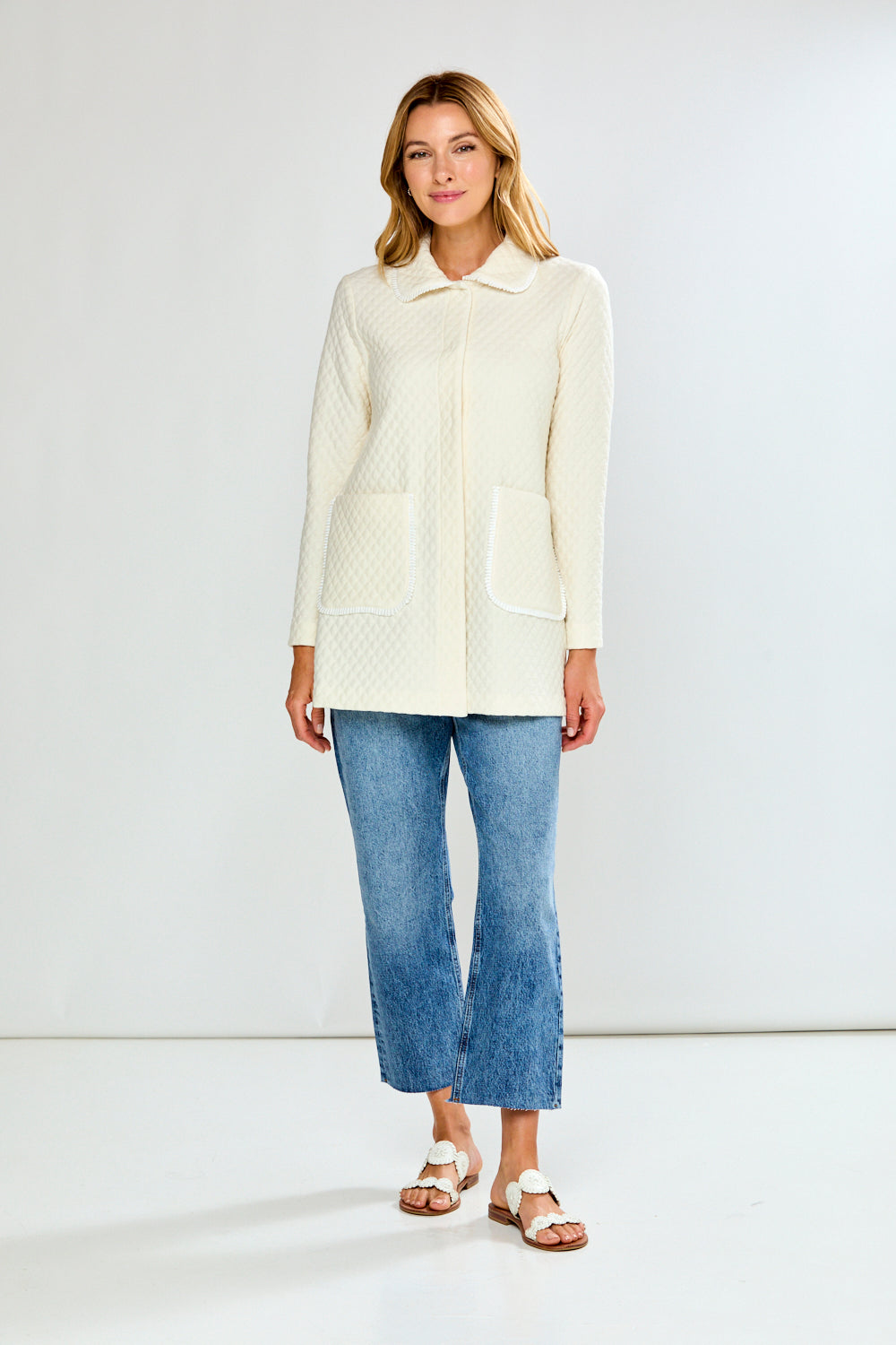 Woman wearing a cream jacket and blue jeans on a white background