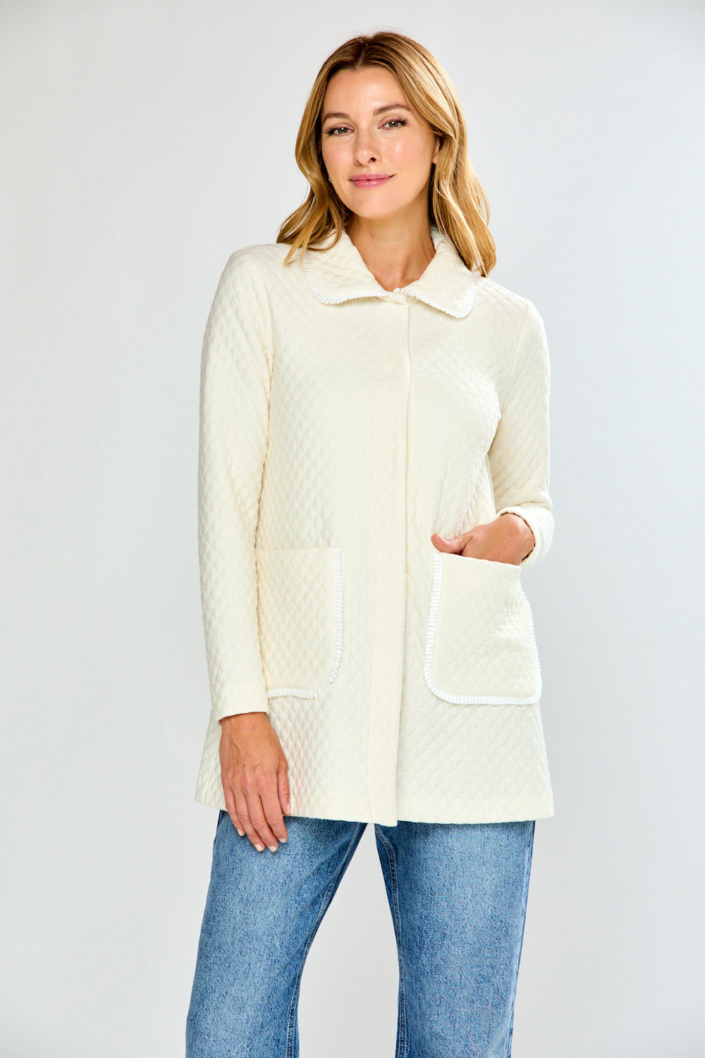 Woman wearing a cream-colored jacket and blue jeans on a white background