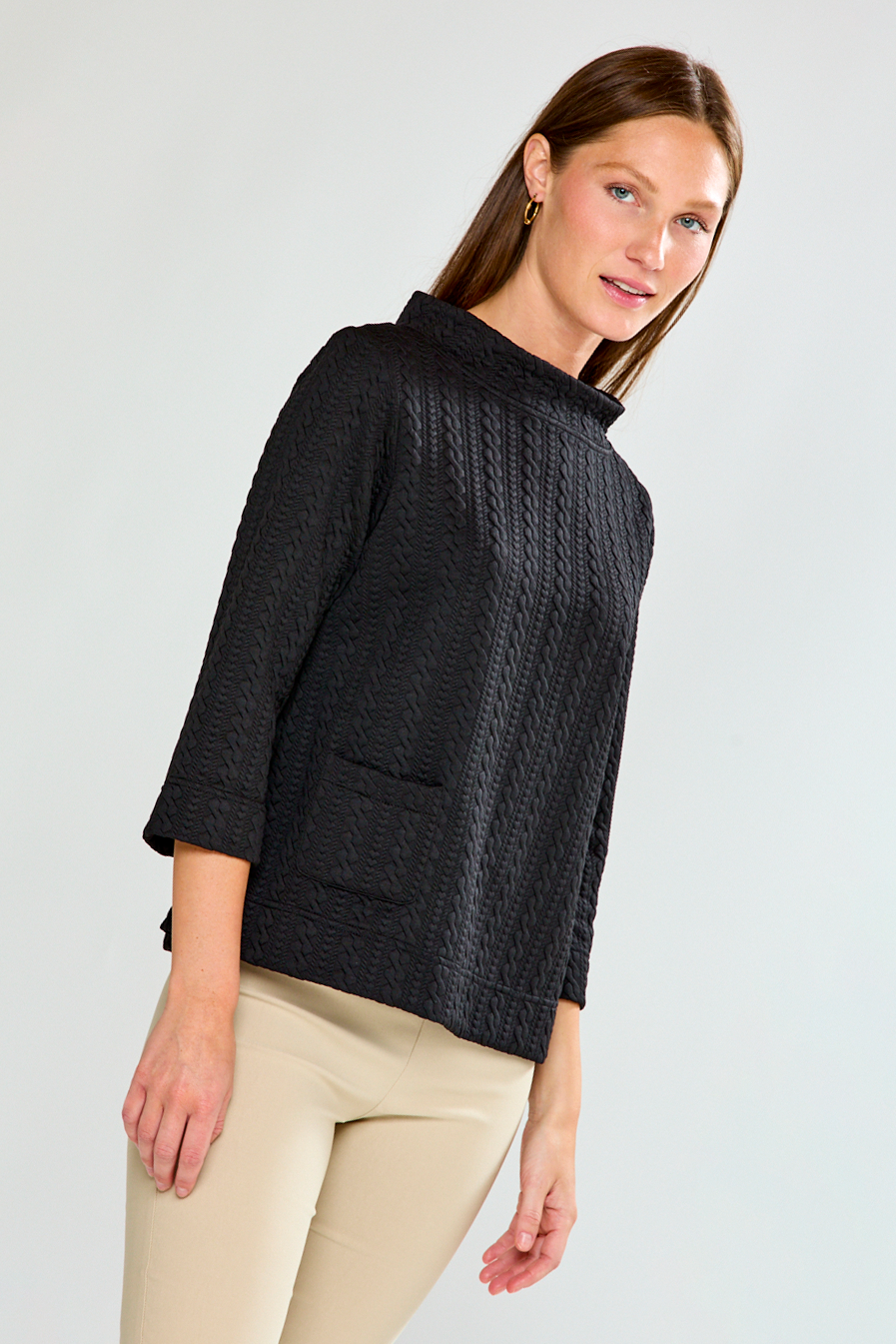 Woman wearing a black textured top and beige pants against a white background
