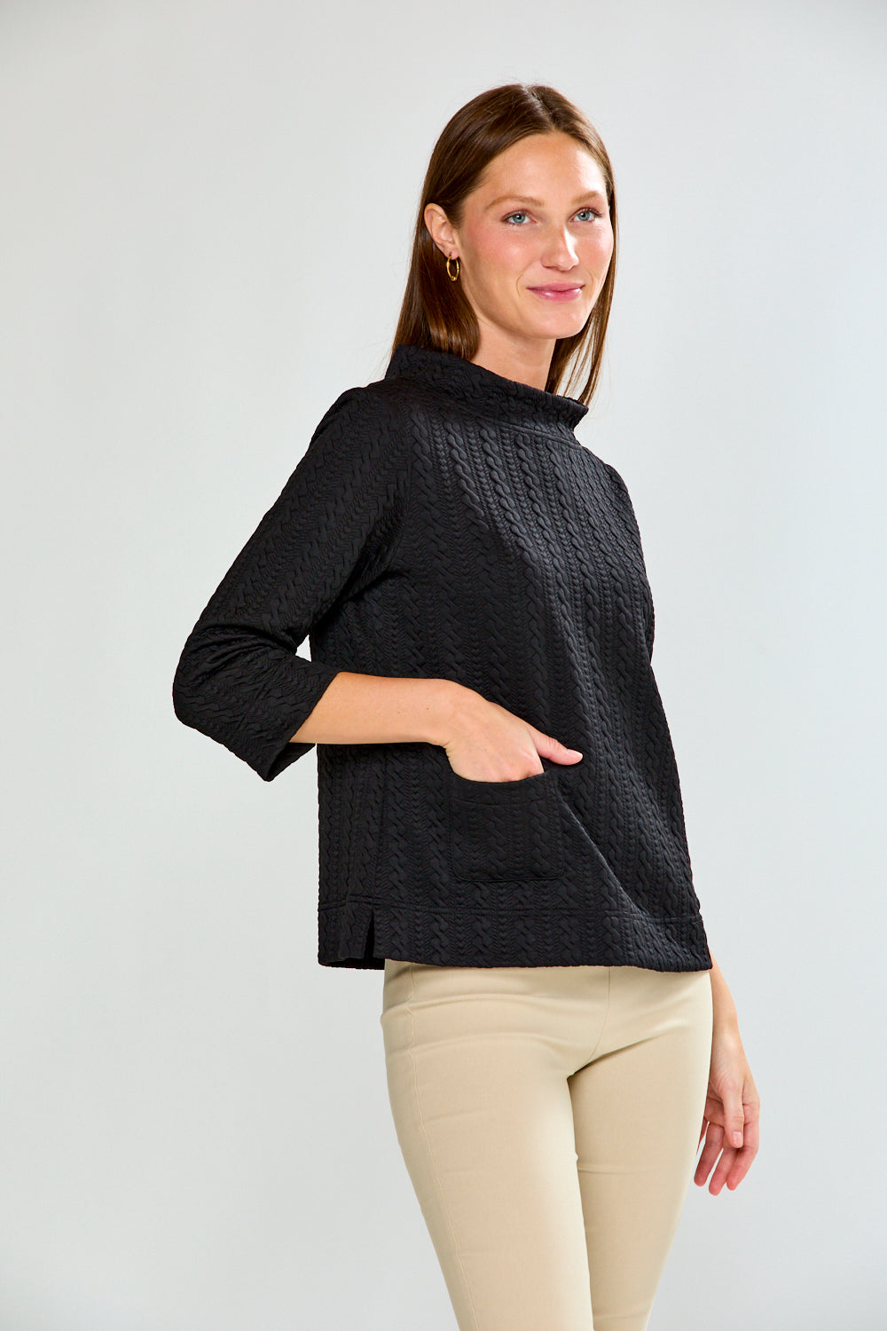 Woman wearing a black textured top and beige pants against a white background