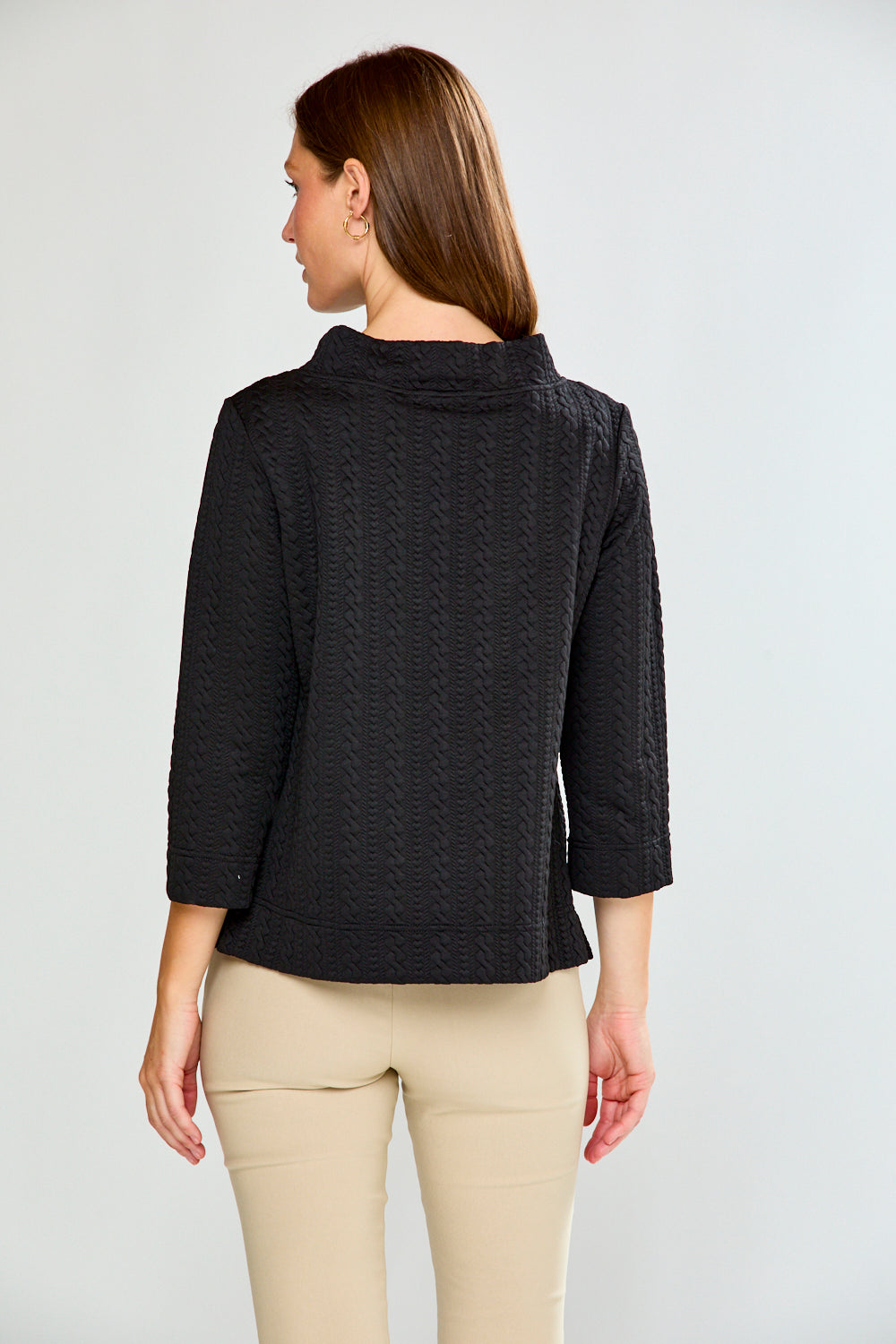 Woman wearing a black textured top and beige pants against a white background