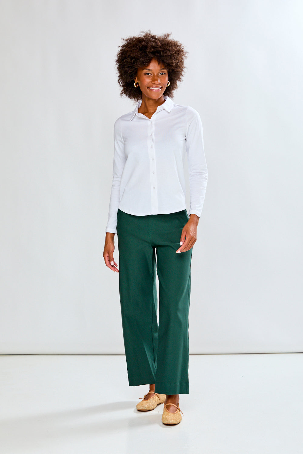 Woman wearing a white shirt and green pants against a plain background